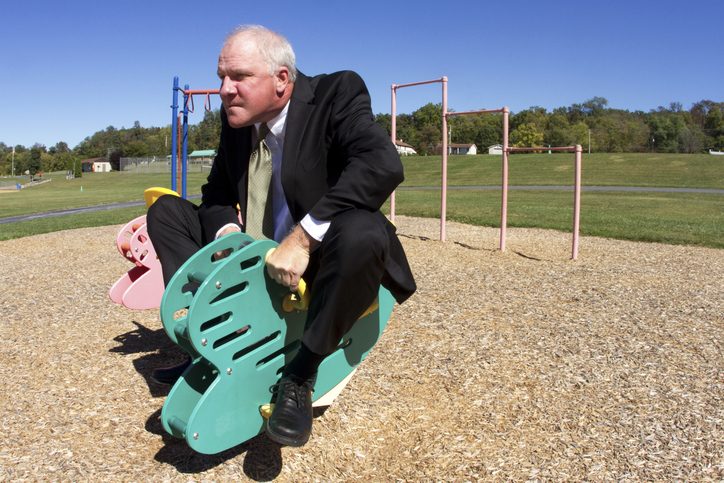 Businessman dressed in suit playing on a ride at a playground