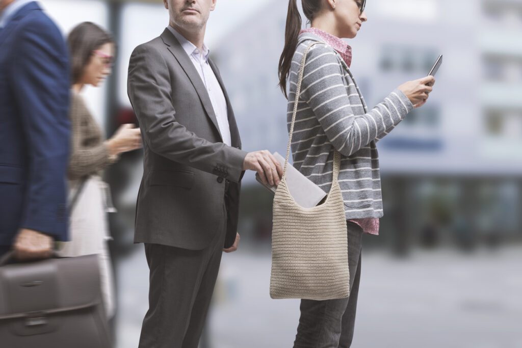 Robber stealing a wallet in the city street, the victim is distracted and using her smartphone